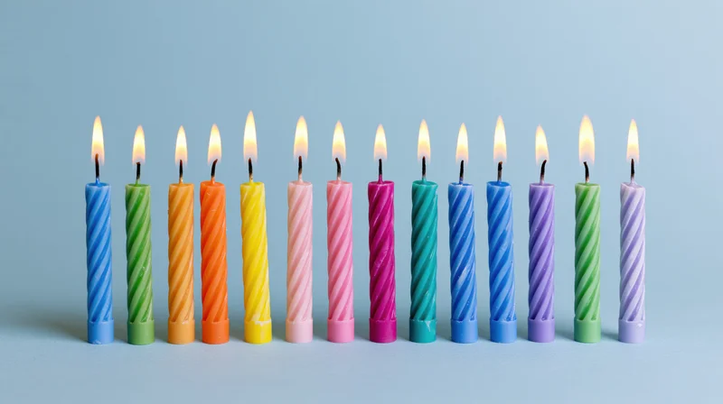 Twelve lit colorful spiral birthday candles arranged in a row on a light blue surface