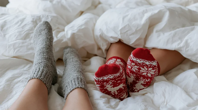 Two pairs of feet in socks peeking from under rumpled white bedding