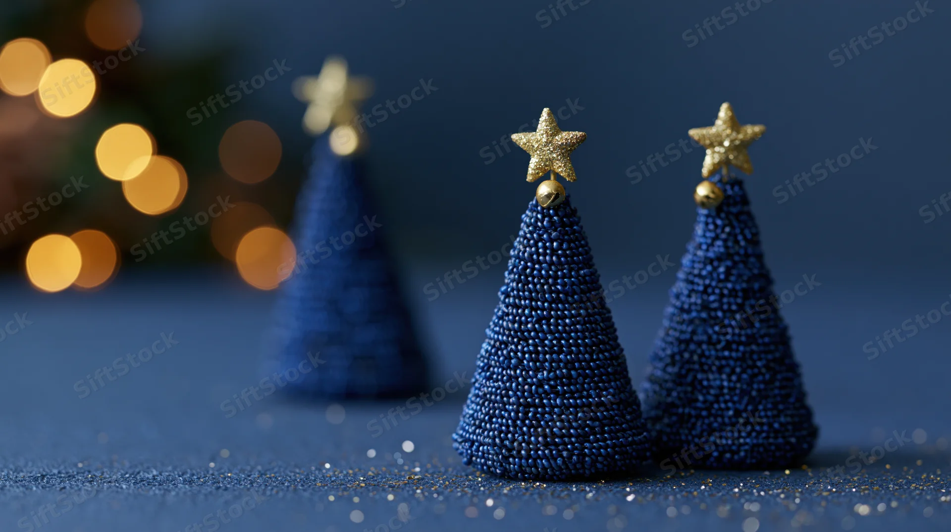 Three blue beaded christmas trees with gold stars on a dark surface near blurred holiday lights
