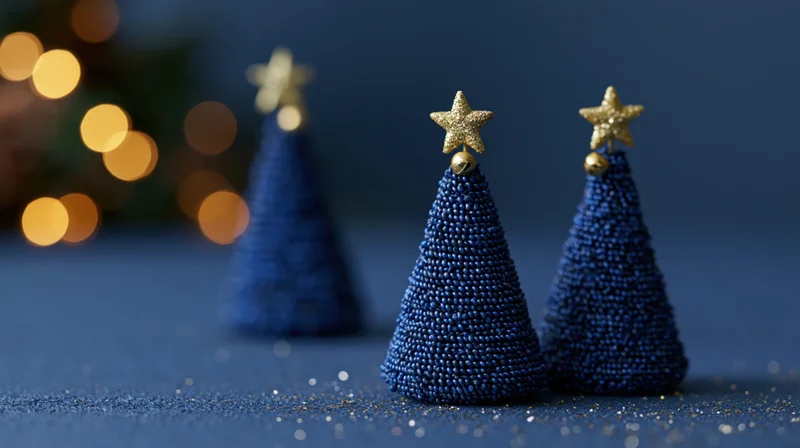 Three blue beaded christmas trees with gold stars on a dark surface near blurred holiday lights