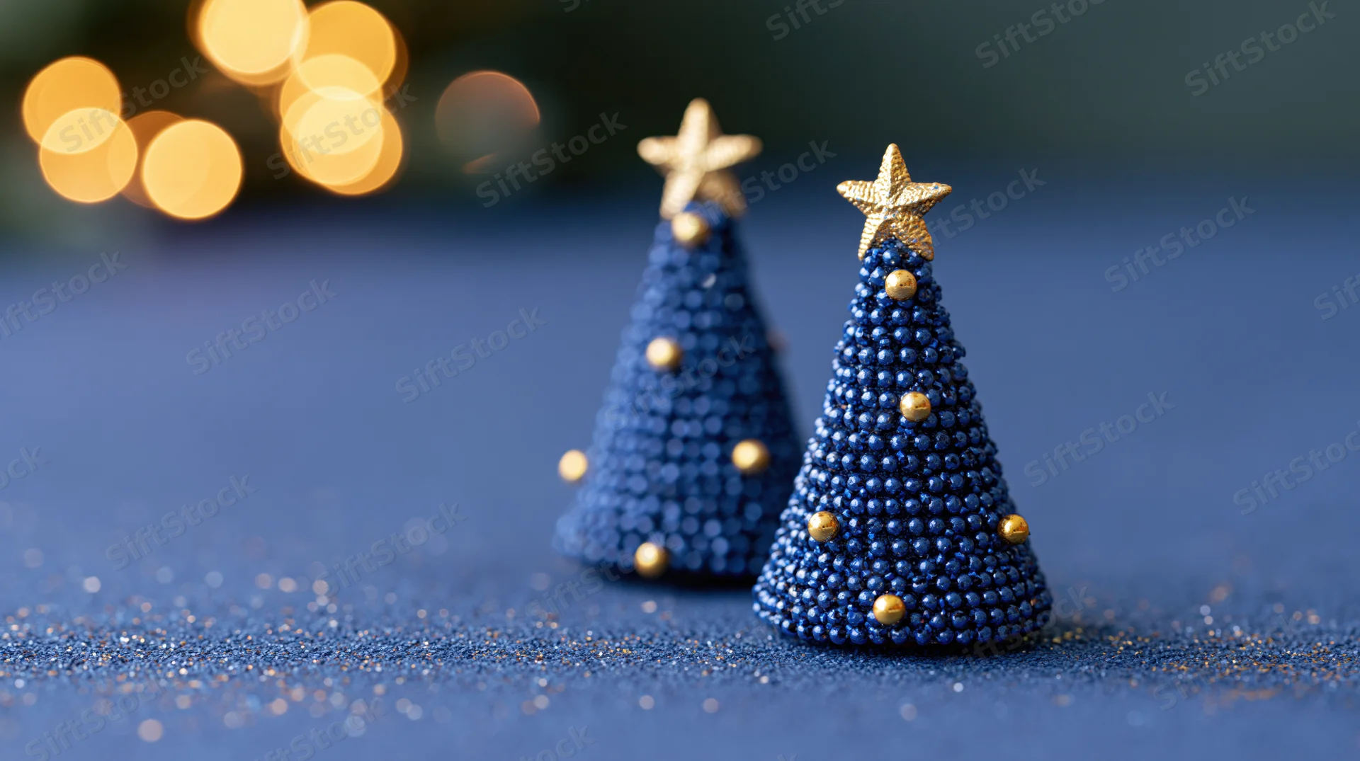 Two small blue beaded christmas trees with gold stars on a glittery blue surface