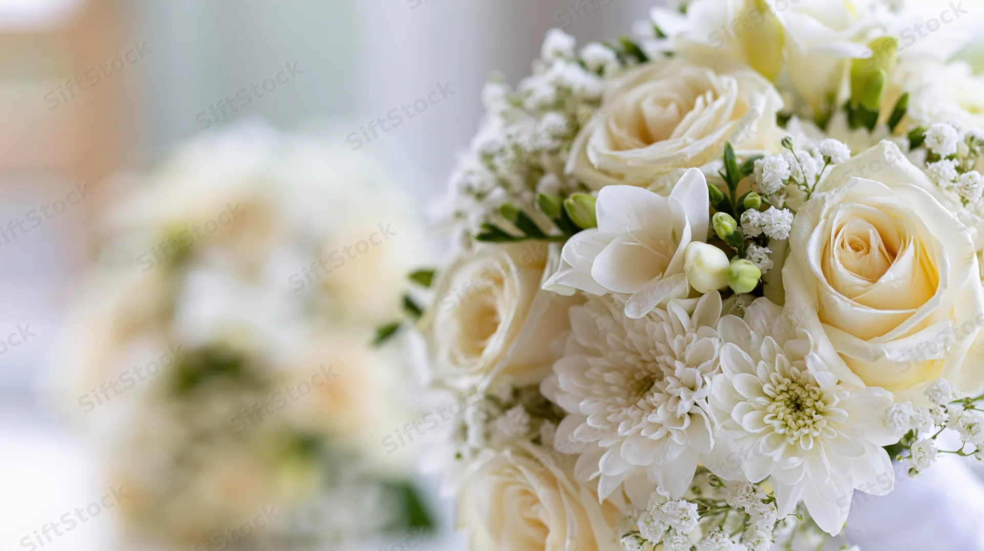 Close-up of a white bridal bouquet with cream roses, chrysanthemums and freesia, arranged with greenery and baby's breath