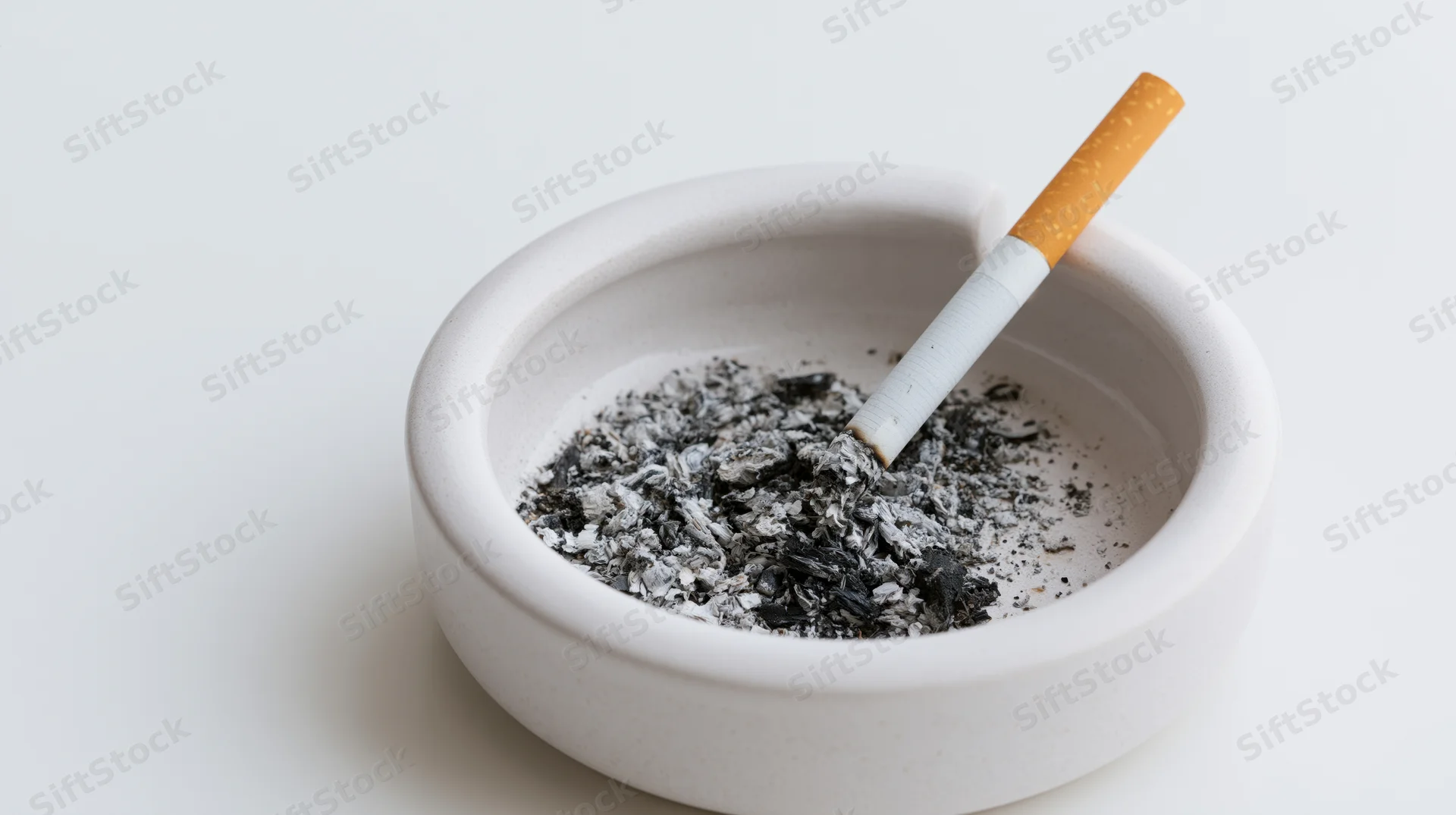 Half-smoked cigarette resting in a white ceramic ashtray filled with ash
