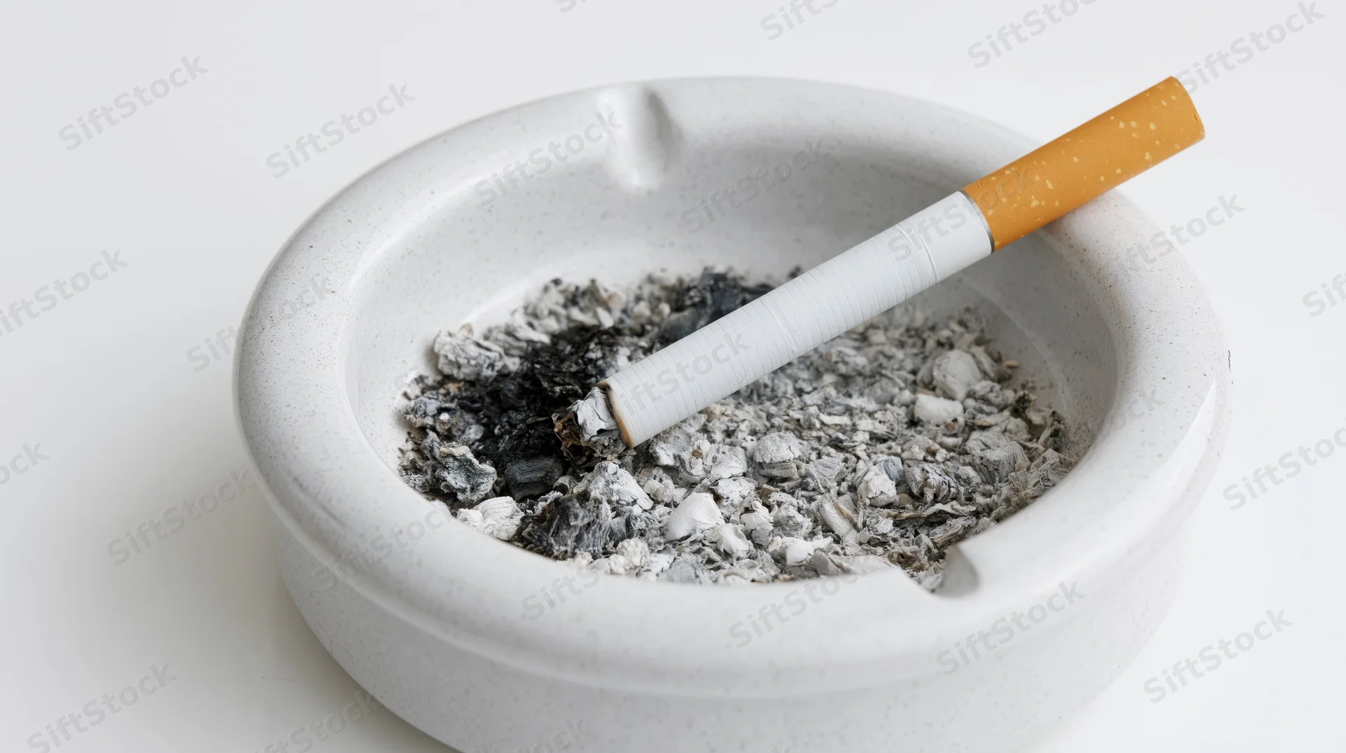 Half-smoked cigarette resting in a white ceramic ashtray filled with ash