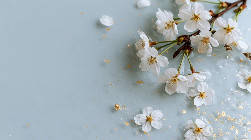 Cherry blossom branch with scattered petals and golden glitter on a light blue surface