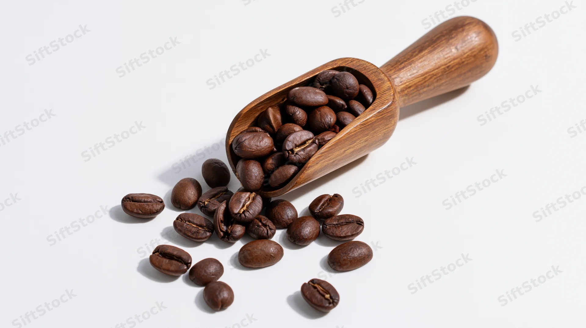 Roasted coffee beans spilling from a wooden scoop on a white surface