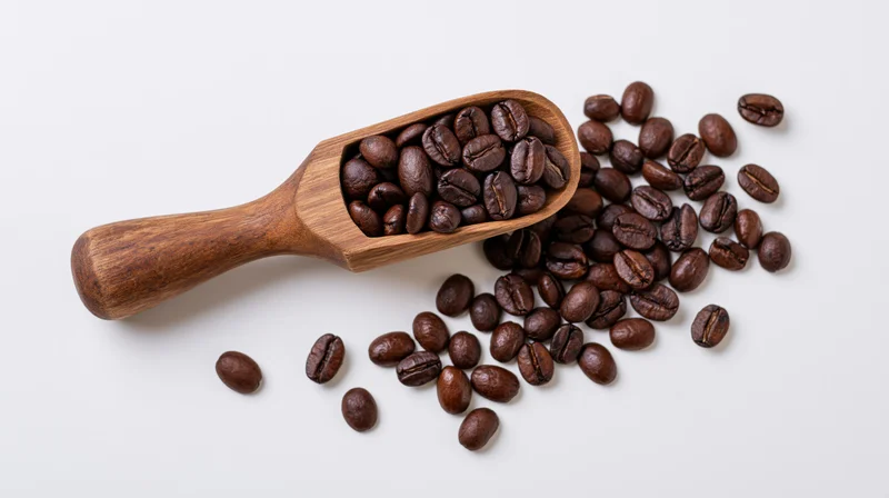 Wooden scoop filled with roasted coffee beans spilling onto white surface
