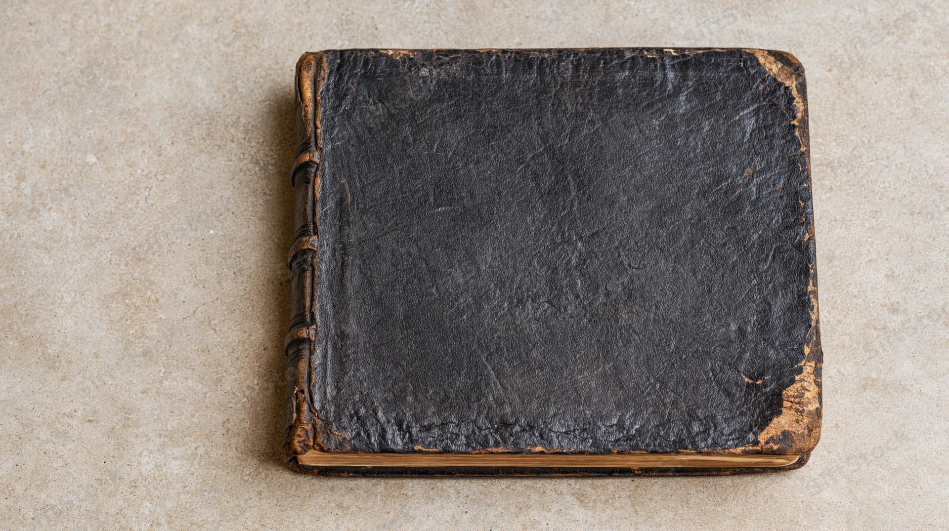 Worn antique leather book lying flat on a textured beige surface