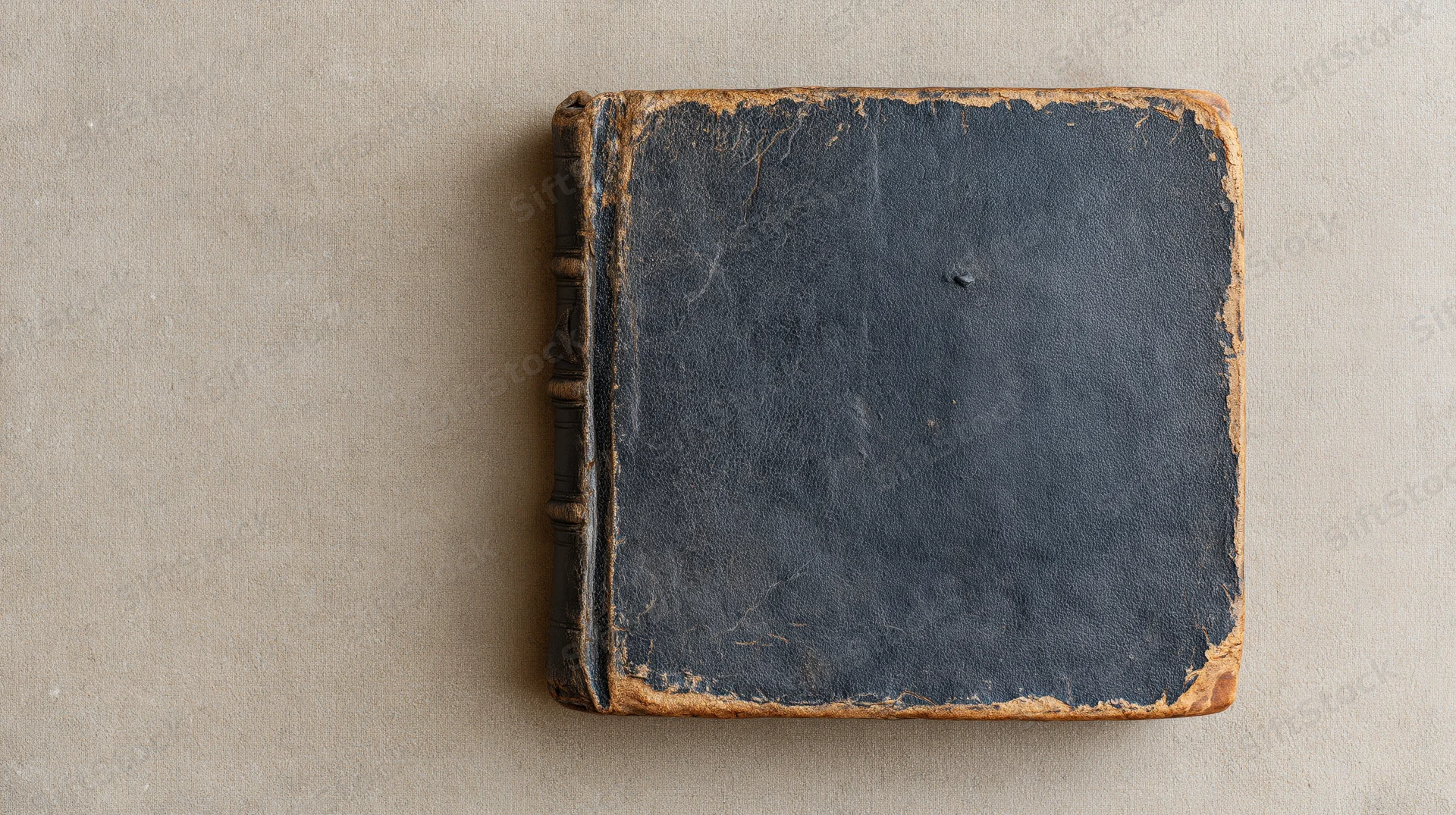 Worn antique hardcover book lying flat on a muted beige textured surface