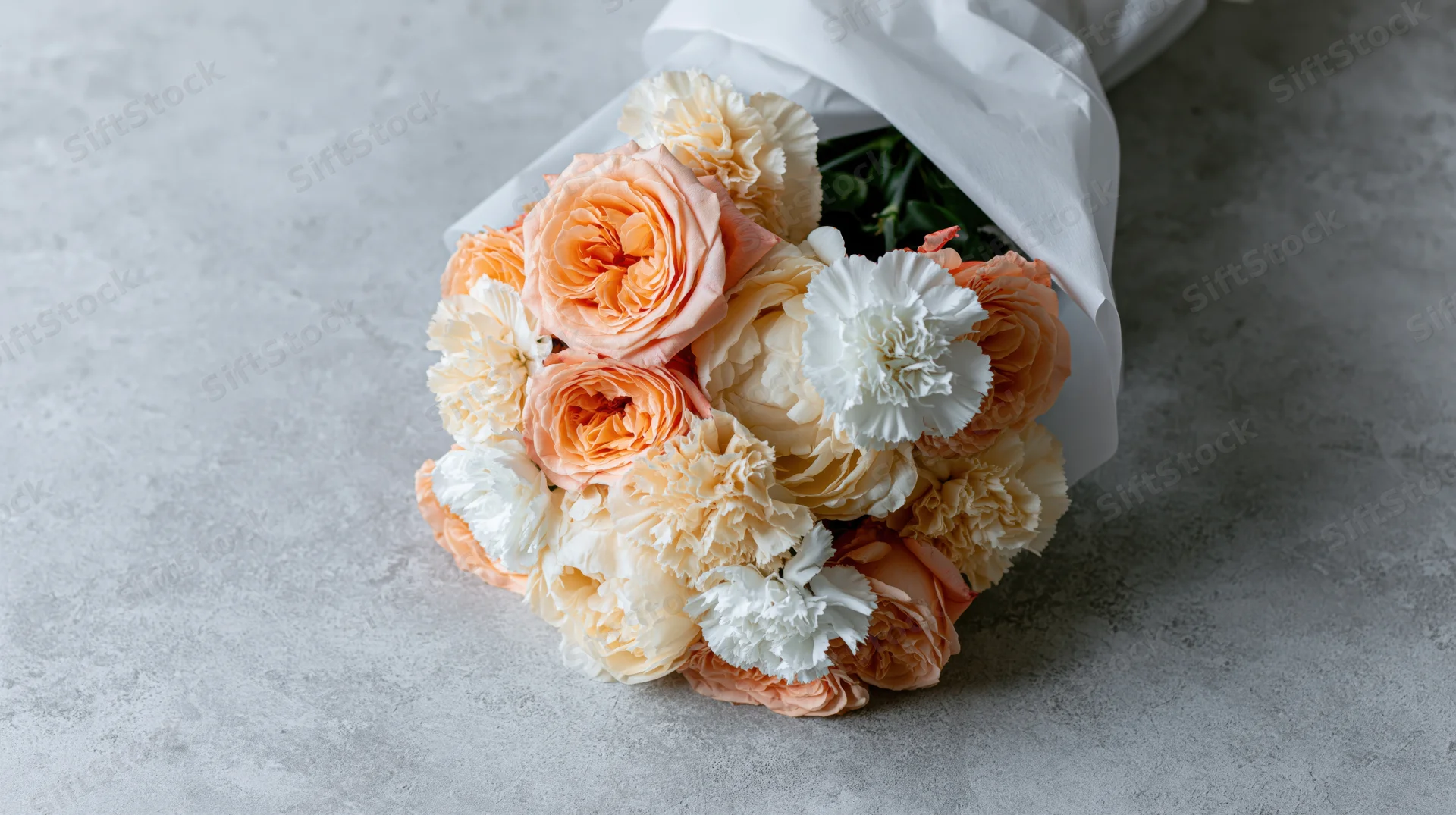 Bouquet of peach roses, cream peonies and white carnations wrapped in paper on a concrete surface