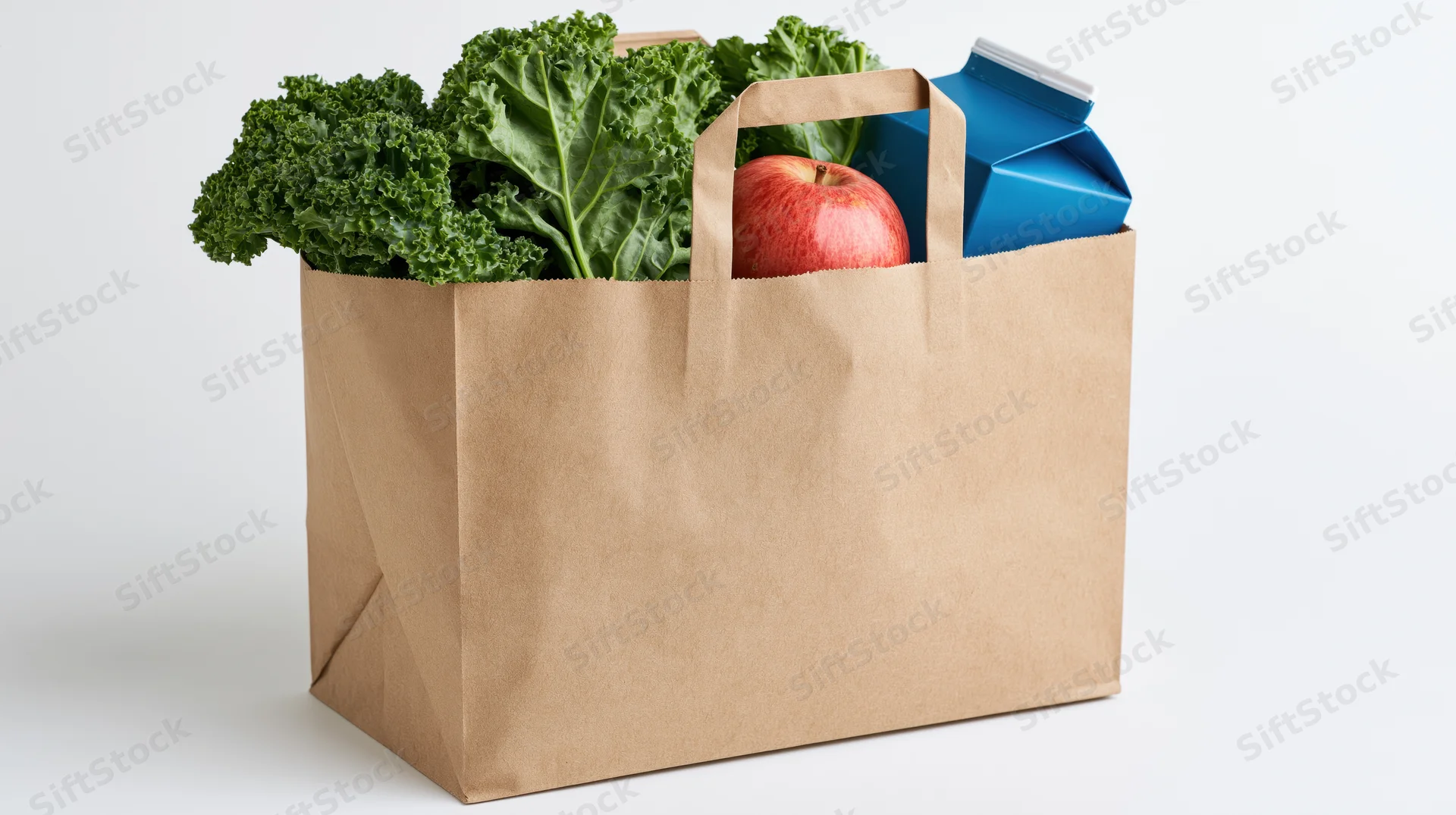 Brown paper grocery bag filled with fresh kale and a red apple on white background