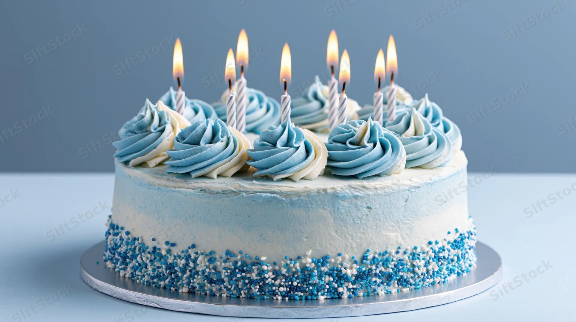 Round birthday cake with blue and white buttercream frosting and lit candles on a silver stand