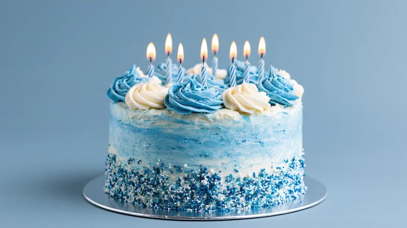 Birthday cake with lit candles and blue white frosting on a silver stand