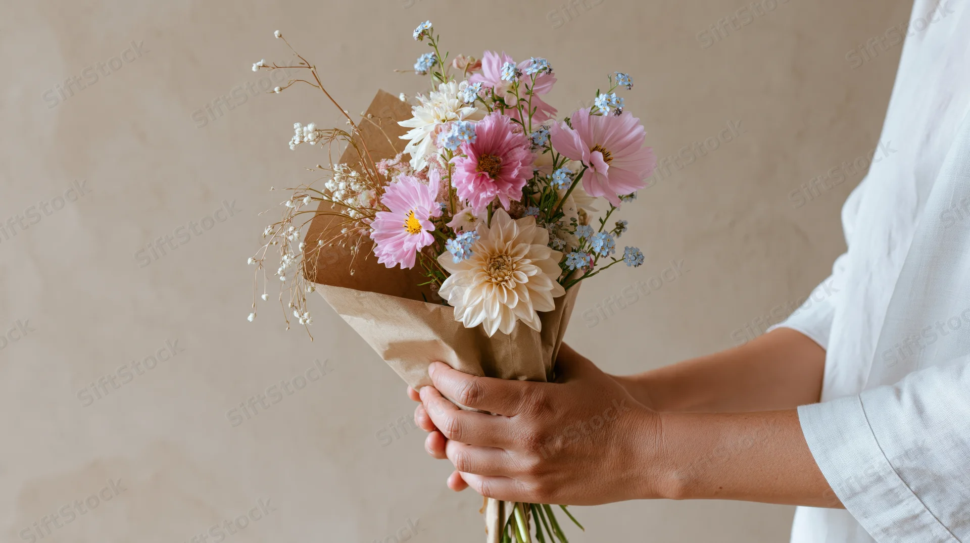 Woman holding a small wildflower bouquet wrapped in brown paper against a neutral wall