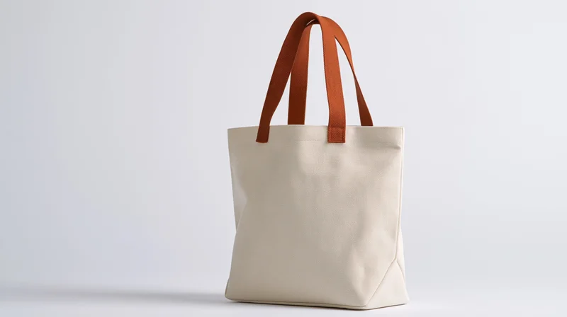 Plain canvas tote bag with burnt orange handles standing on white background