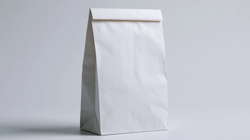Plain white paper bag standing upright on a neutral surface with blank front for branding or design application