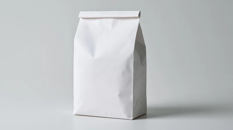 Plain white paper bag standing upright on a neutral surface with blank front for branding or design application
