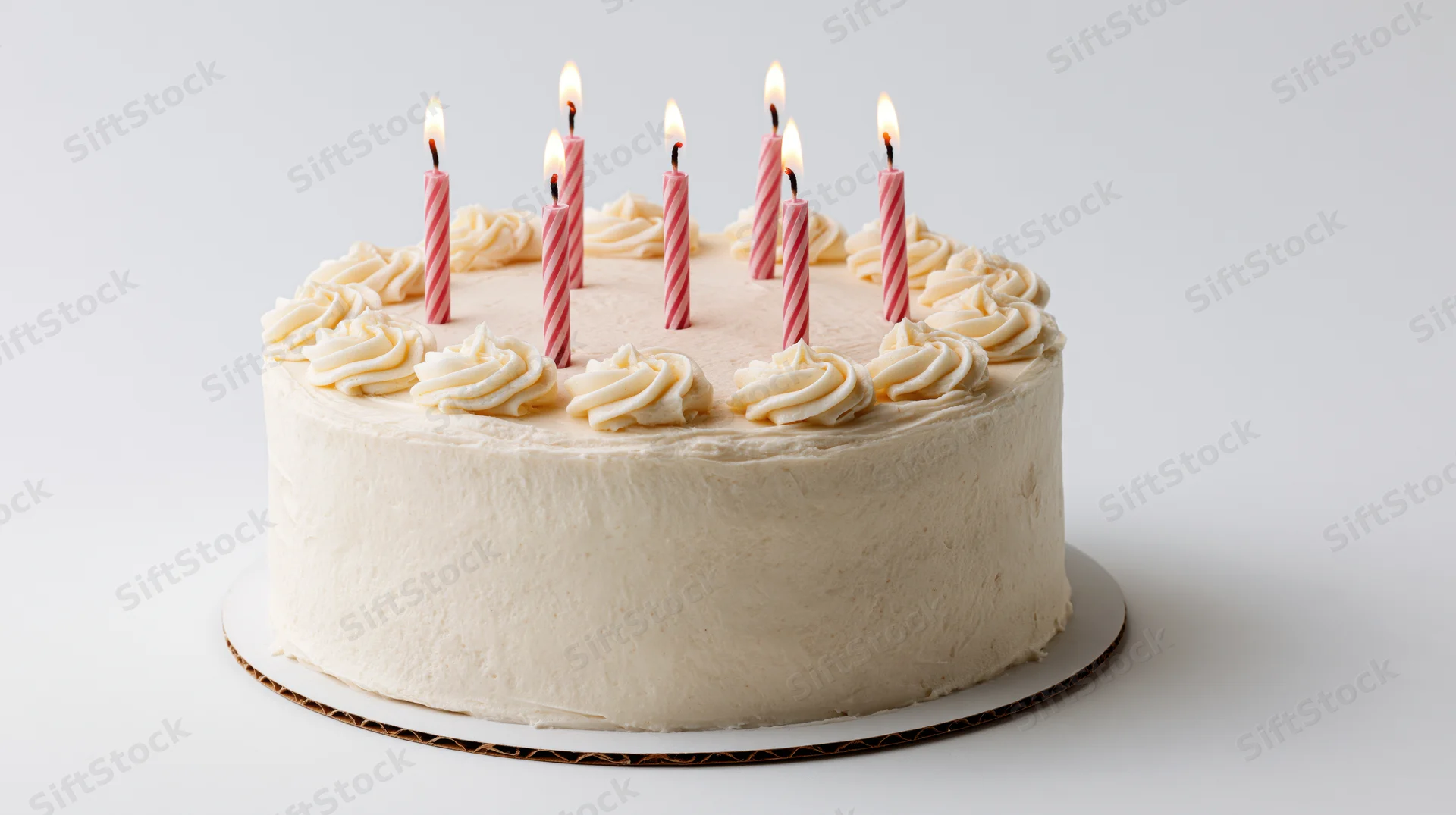 Round white frosted birthday cake with seven lit pink candles on a cake stand against a white background