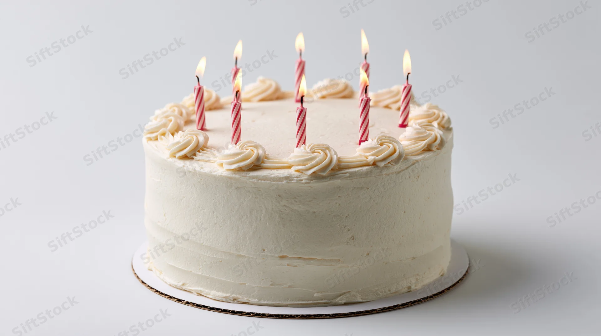Round white frosted birthday cake with seven lit pink and white striped candles on a white surface