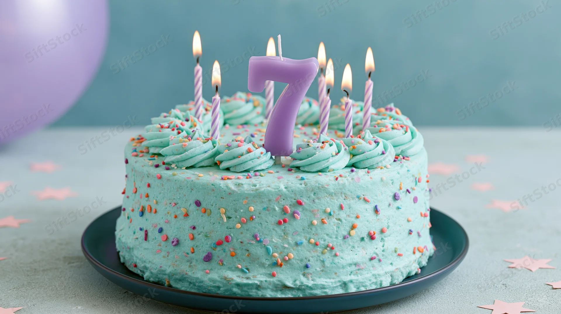 Turquoise birthday cake with lit candles and number seven candle on a plate, surrounded by star confetti and a purple balloon