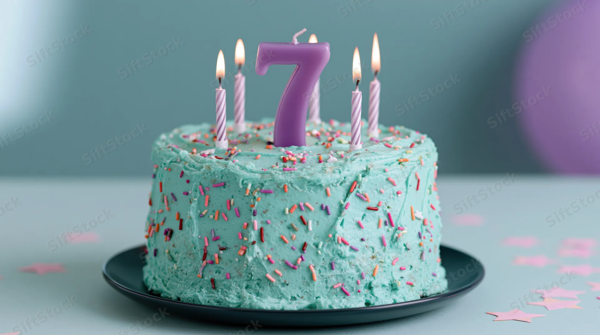 Turquoise frosted birthday cake with number seven candle and lit candles on a plate surrounded by star confetti
