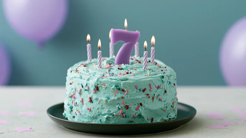 Turquoise frosted birthday cake with number seven candle and sprinkles on a plate, surrounded by balloons and confetti