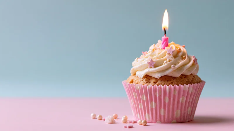 Single birthday cupcake with lit pink candle and frosting on pink surface