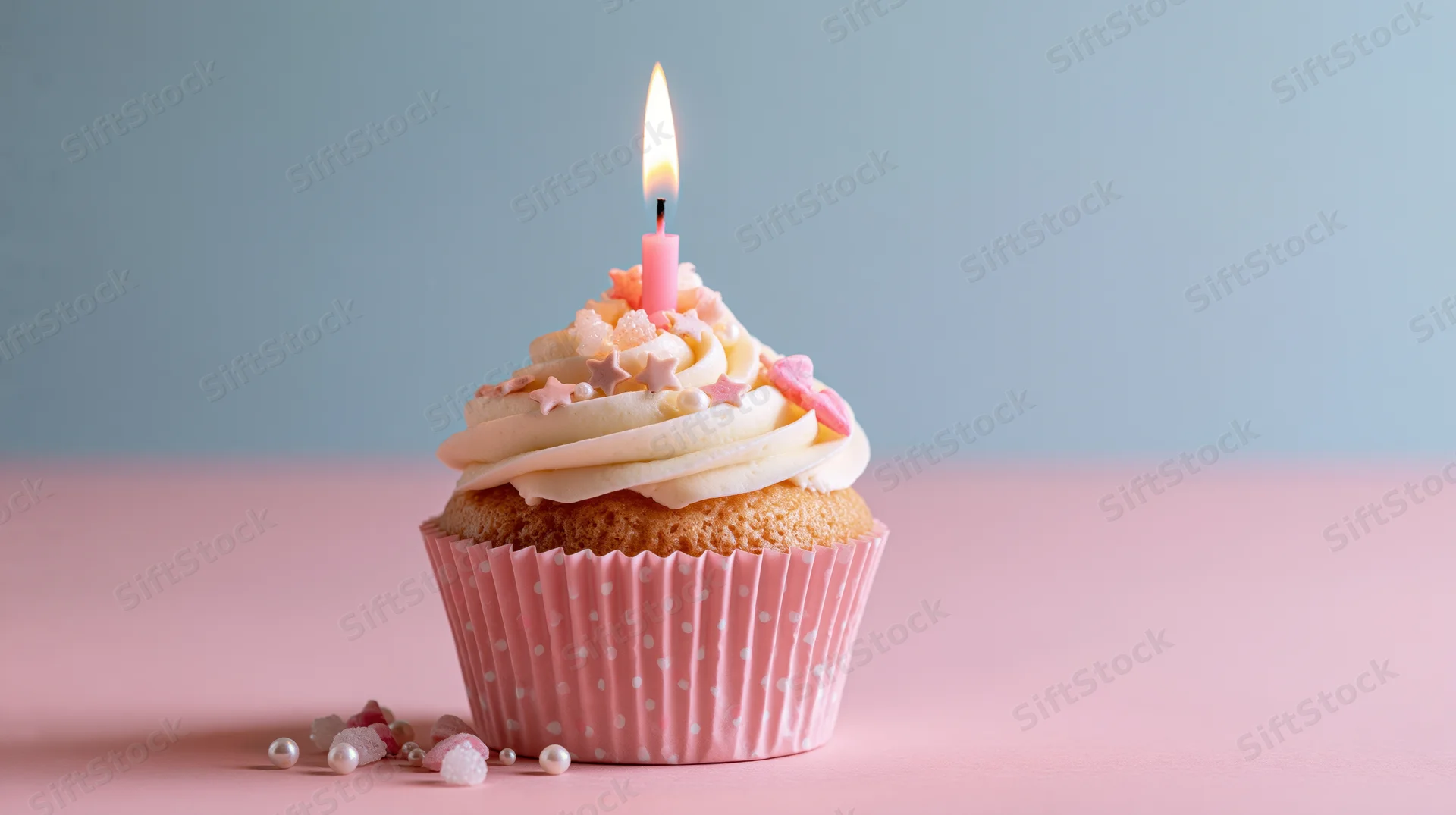 Single birthday cupcake with lit pink candle and star sprinkles on pink surface