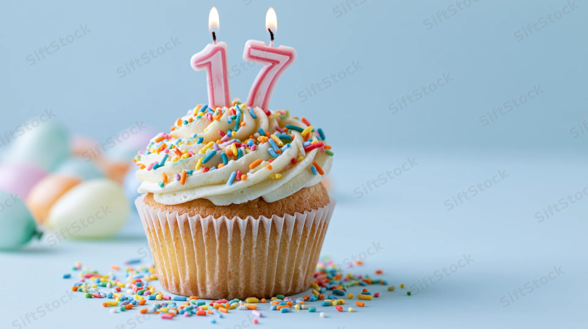 Birthday cupcake with lit number 17 candles and sprinkles on light blue surface