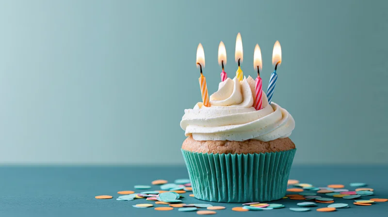 Birthday cupcake with lit candles and confetti on teal surface