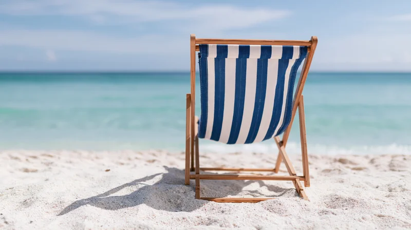 Blue and white striped wooden folding beach chair on sandy shore facing ocean