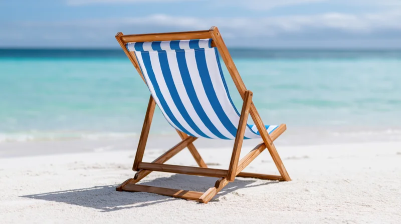 Blue and white striped wooden folding beach chair on sandy shore facing turquoise ocean