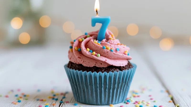 Chocolate cupcake with pink frosting and blue number 7 candle on wooden surface