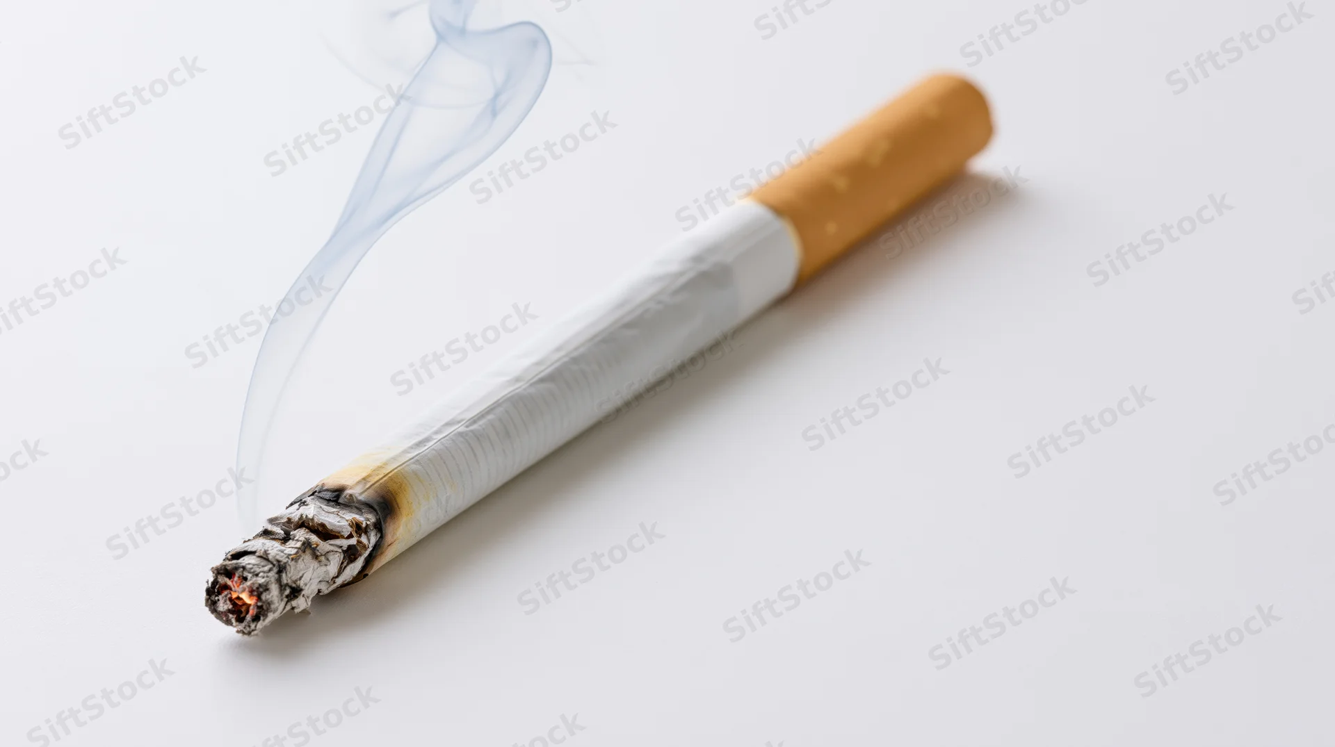 Lit cigarette burning diagonally on white surface with rising smoke