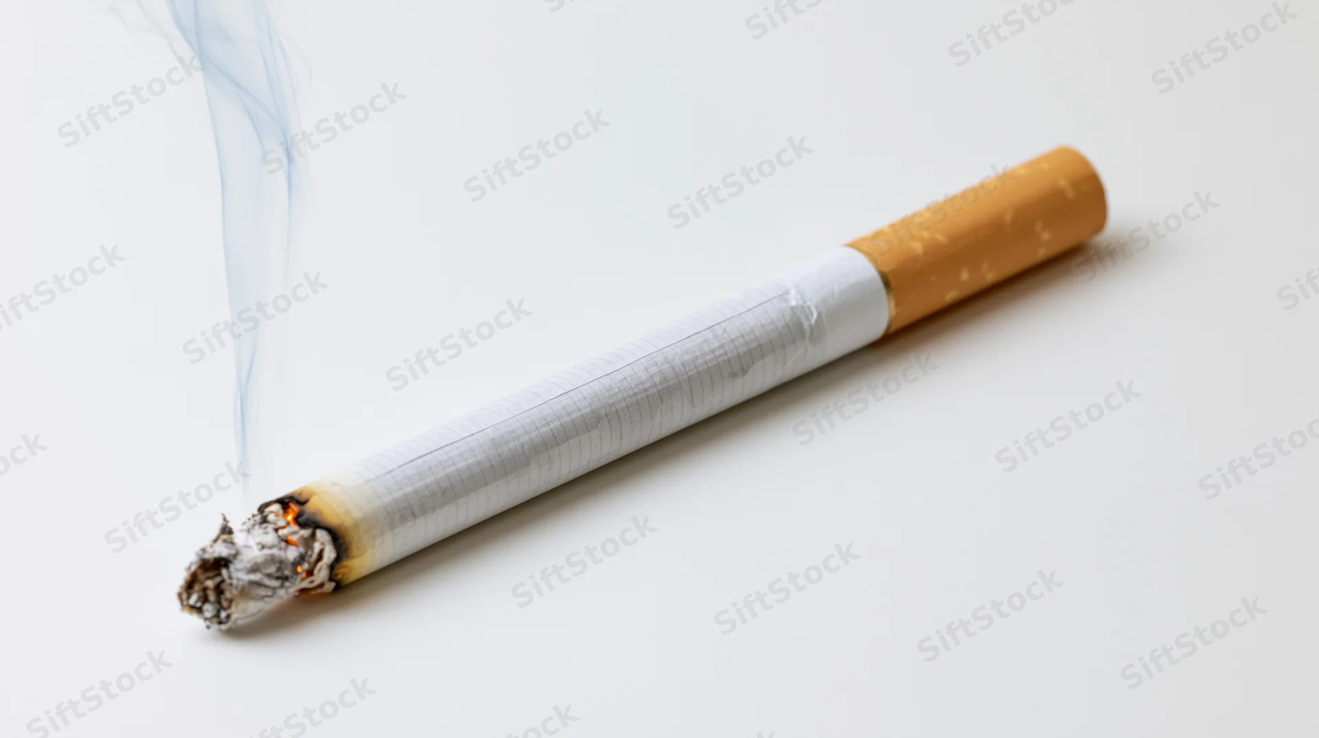 Lit cigarette with smoke and ash resting diagonally on white surface