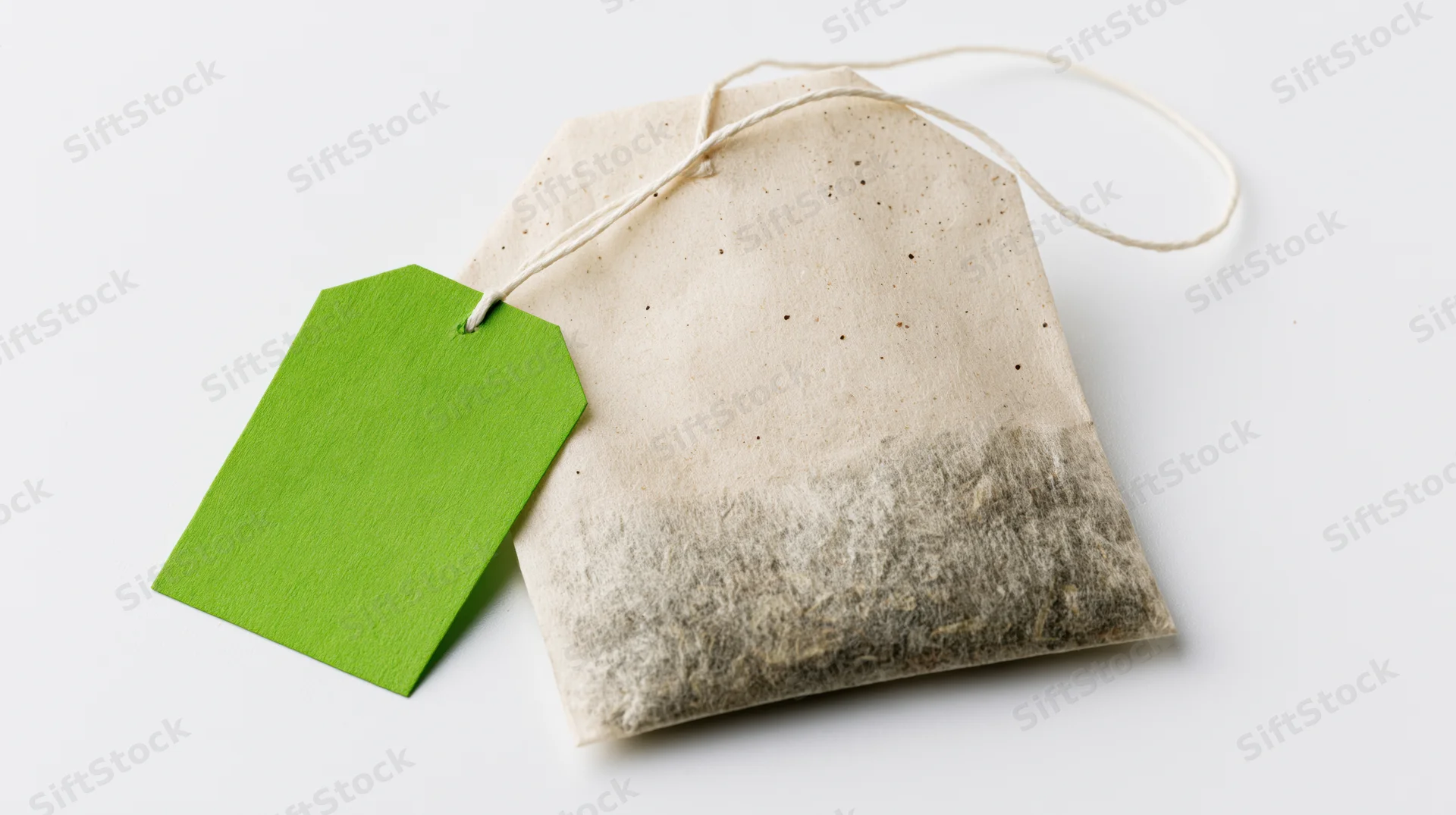 Single unused tea bag with bright green paper tag on white background