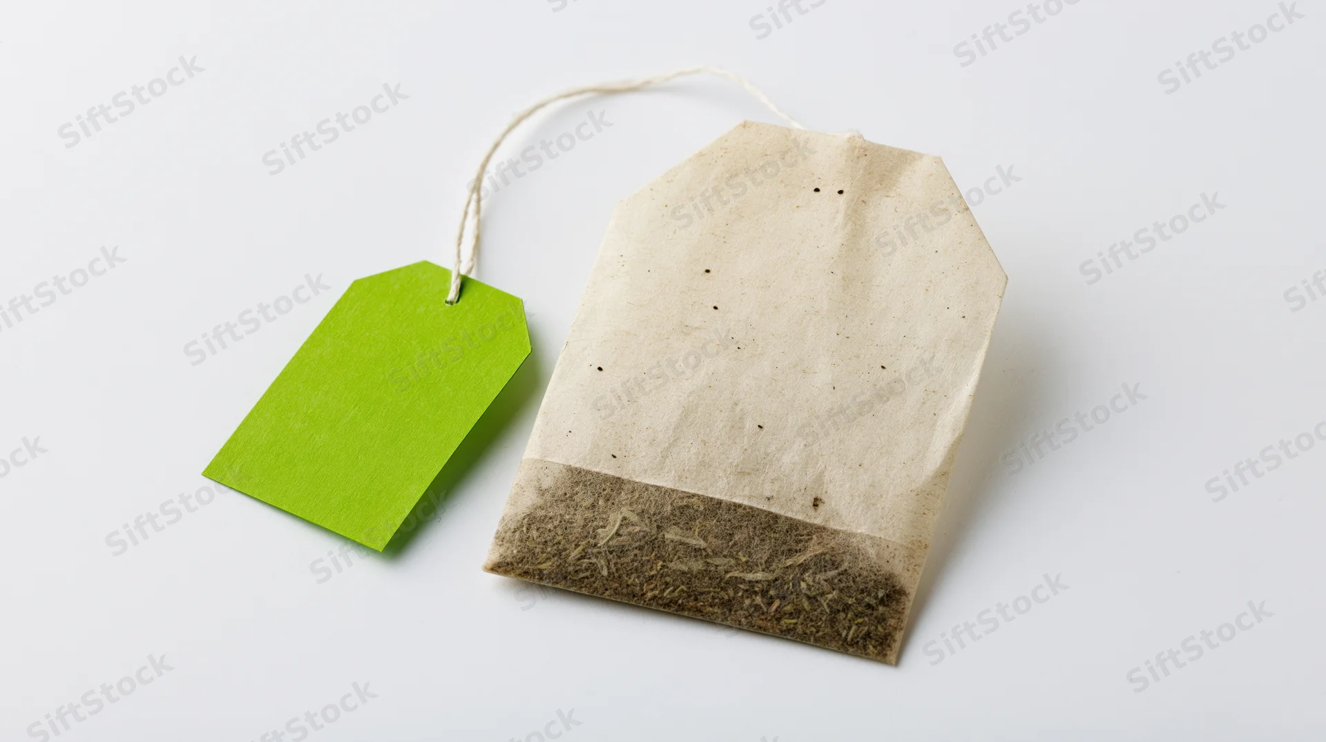 Single unused tea bag with bright green paper tag attached, on white background
