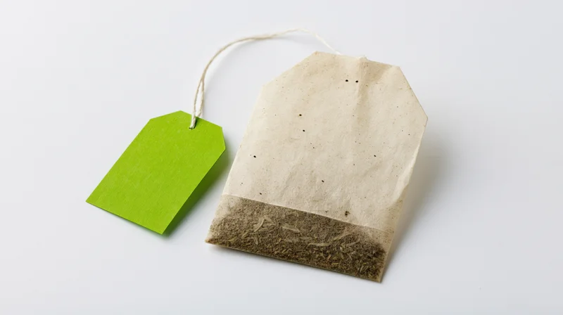 Single unused tea bag with bright green paper tag attached, on white background