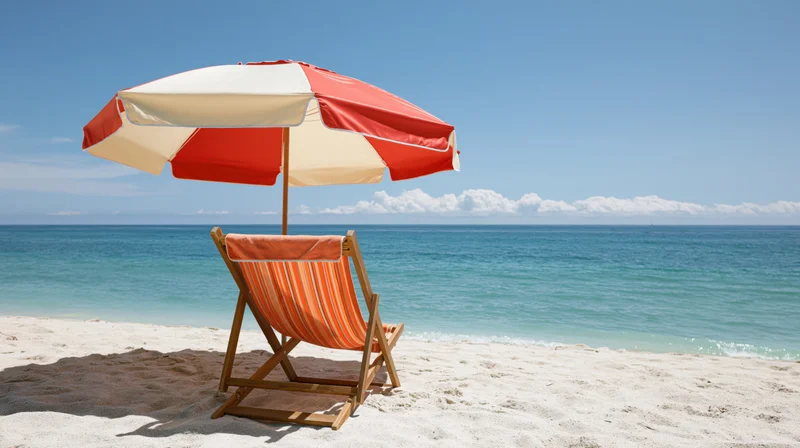 Wooden deck chair with orange-striped fabric under red and white umbrella on sandy beach facing ocean