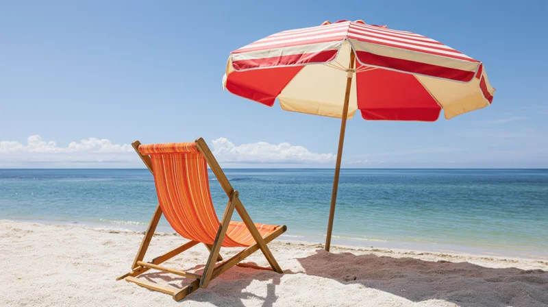Wooden deck chair with orange-striped fabric and red-white striped umbrella on sandy beach by ocean