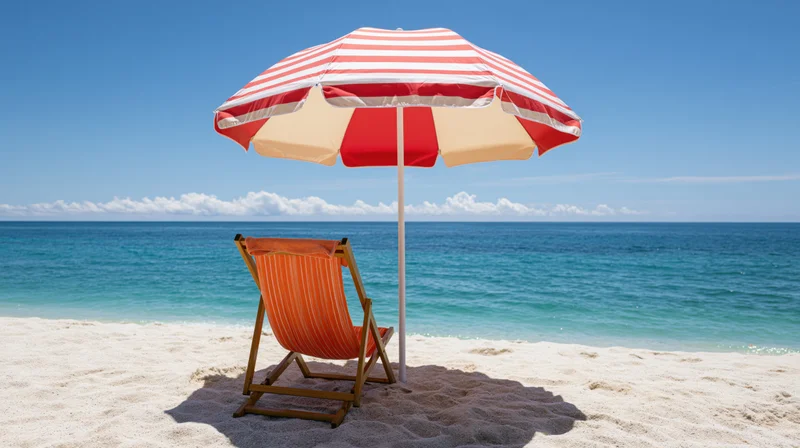 Wooden deck chair with orange-striped fabric under red-and-white striped umbrella on sandy beach facing ocean