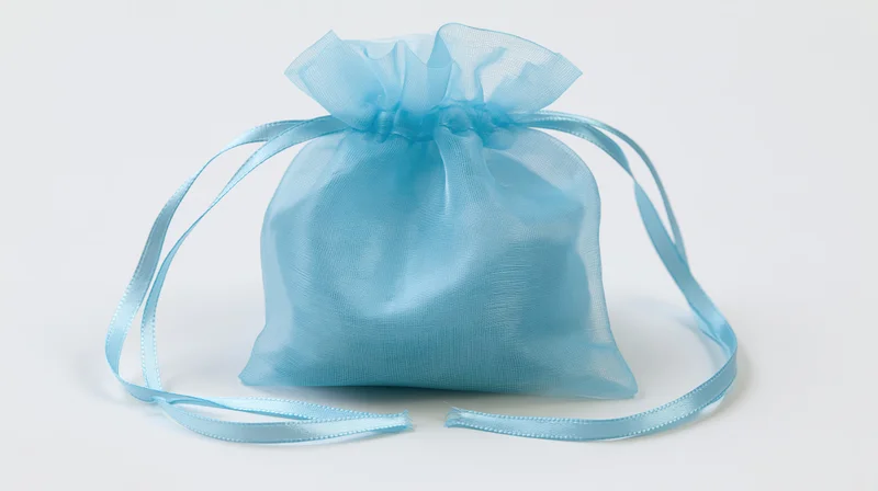 Small light blue organza drawstring gift bag sitting upright on white background