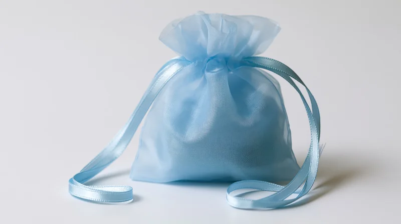 Light blue organza drawstring gift bag sitting upright on white background