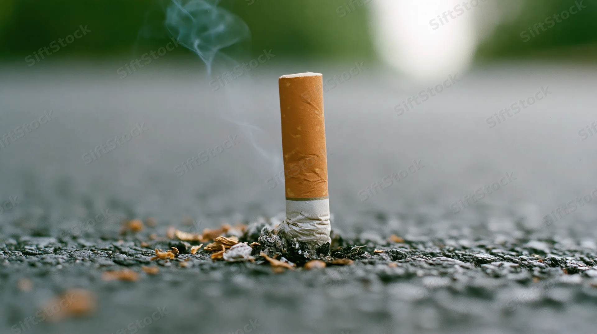 Cigarette butt pressed into dark asphalt with smoke rising