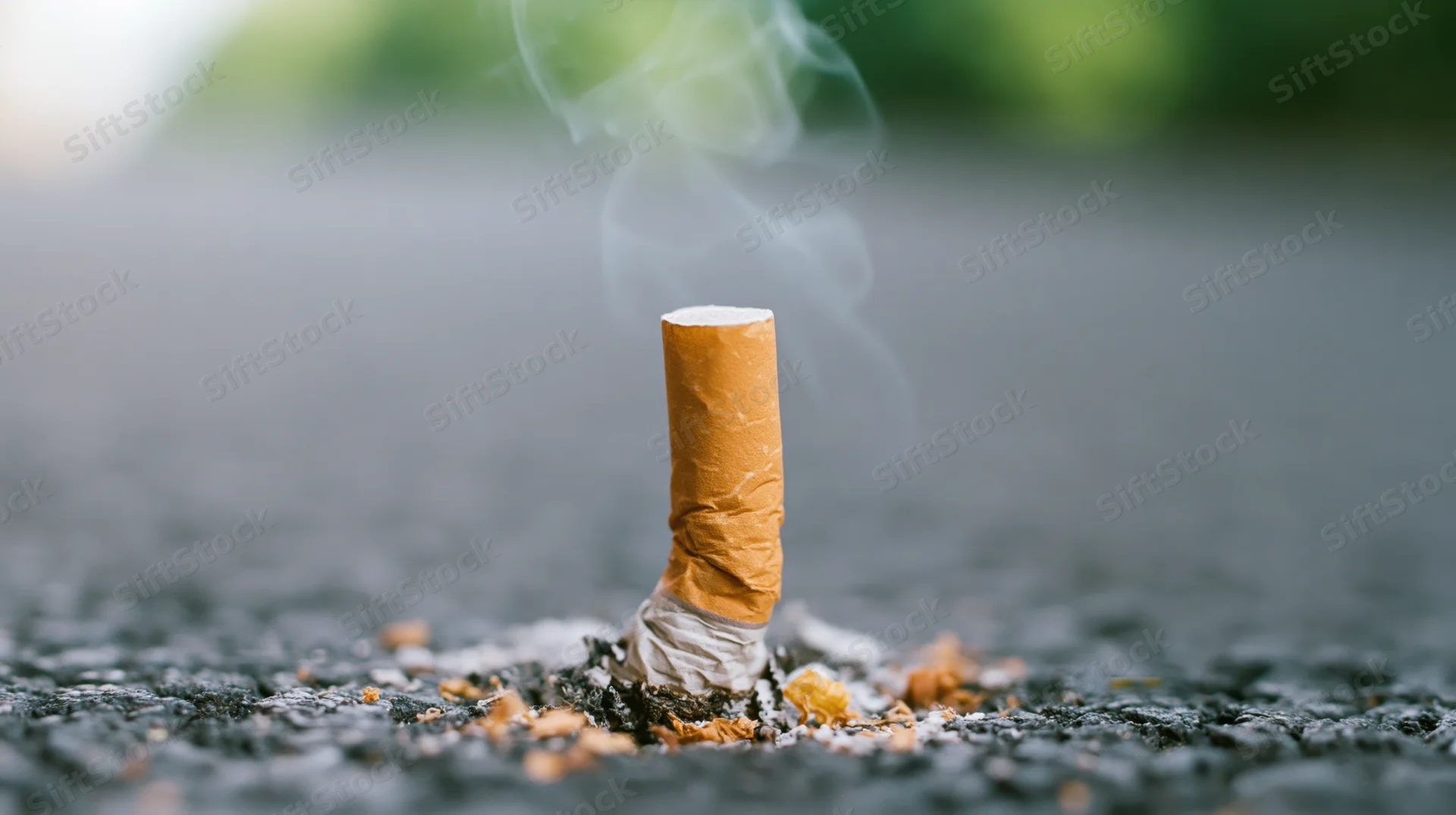 Cigarette butt pressed into dark asphalt with smoke rising