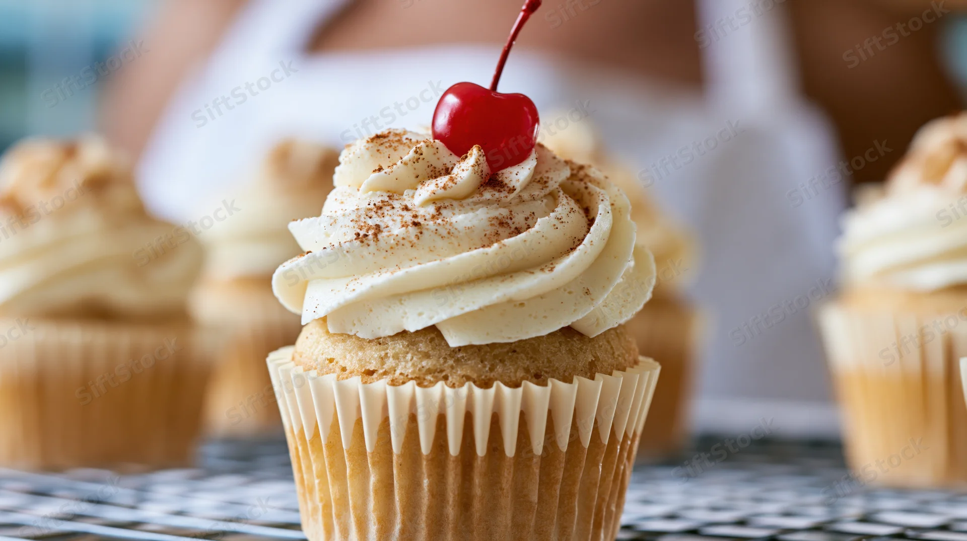 Vanilla cupcake with cream frosting and cherry on top on wire rack