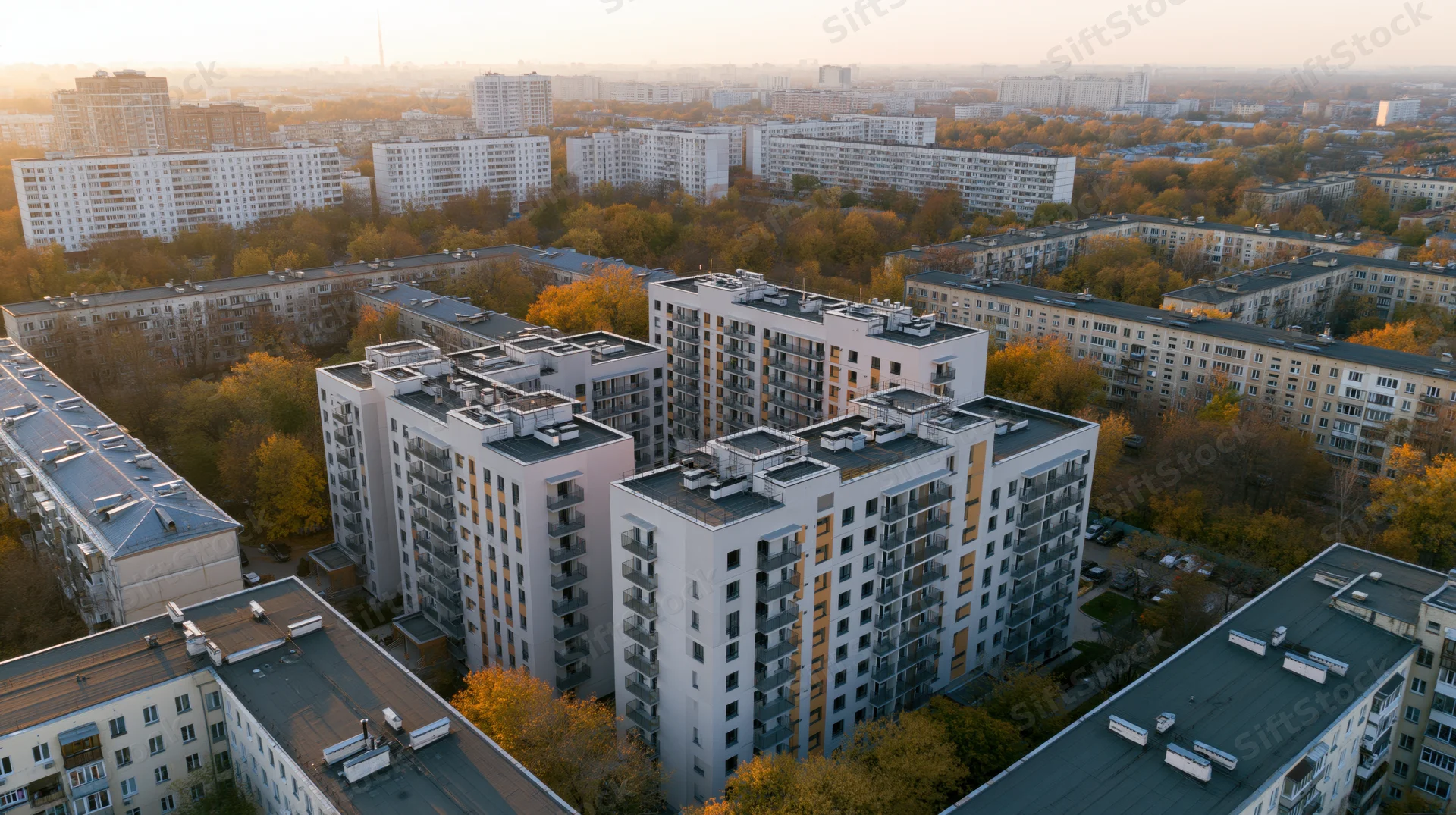 Aerial view of modern apartment buildings in a dense urban neighborhood surrounded by autumn trees at sunset