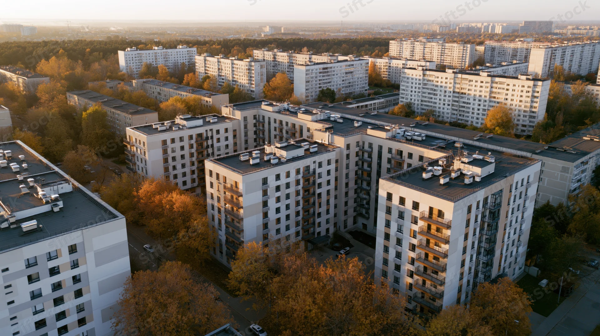 Aerial view of modern apartment buildings in a residential neighborhood surrounded by autumn trees at sunset
