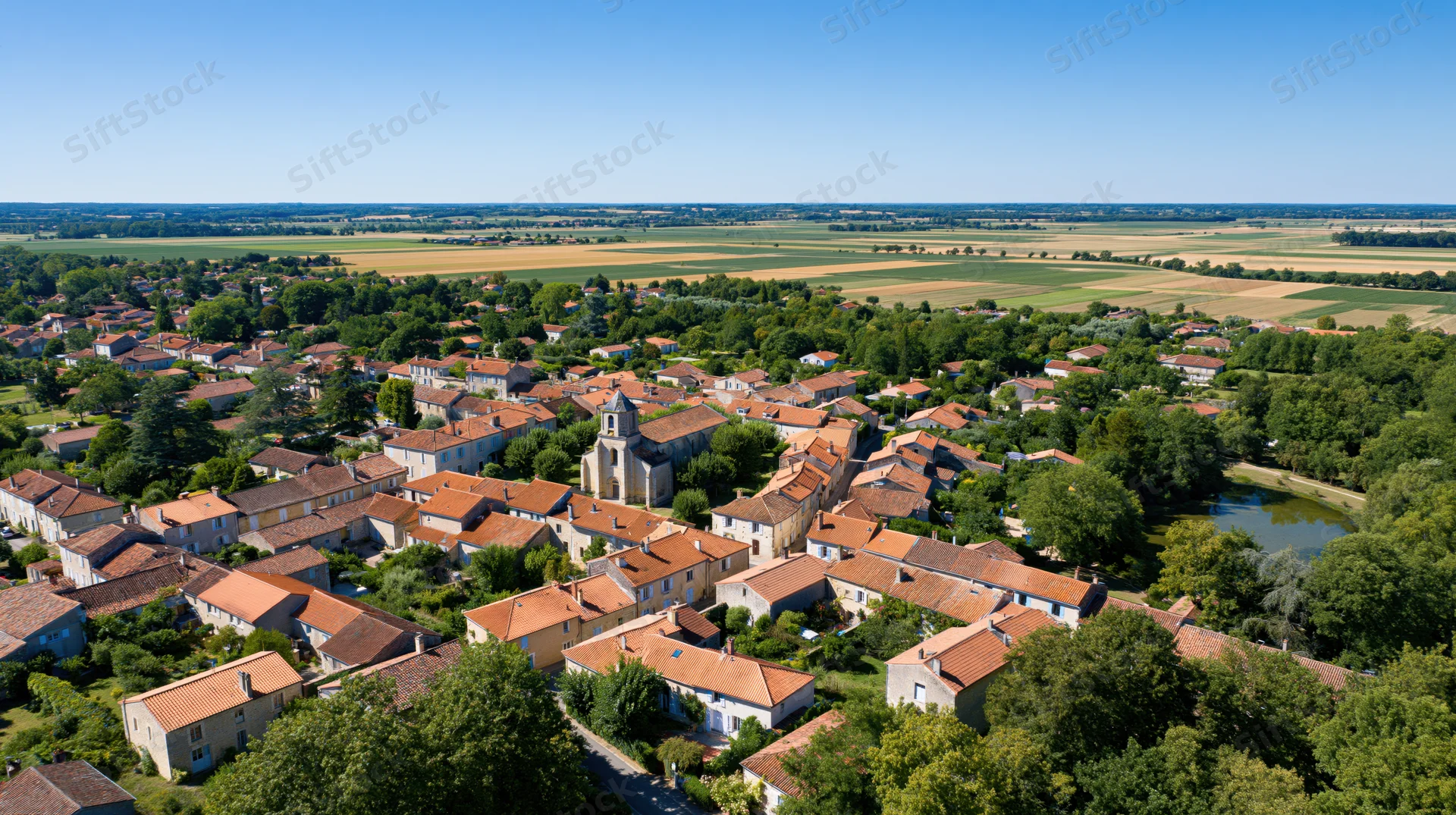 Aerial view of a small french village with red-tiled roofs and a central church surrounded by green fields and trees