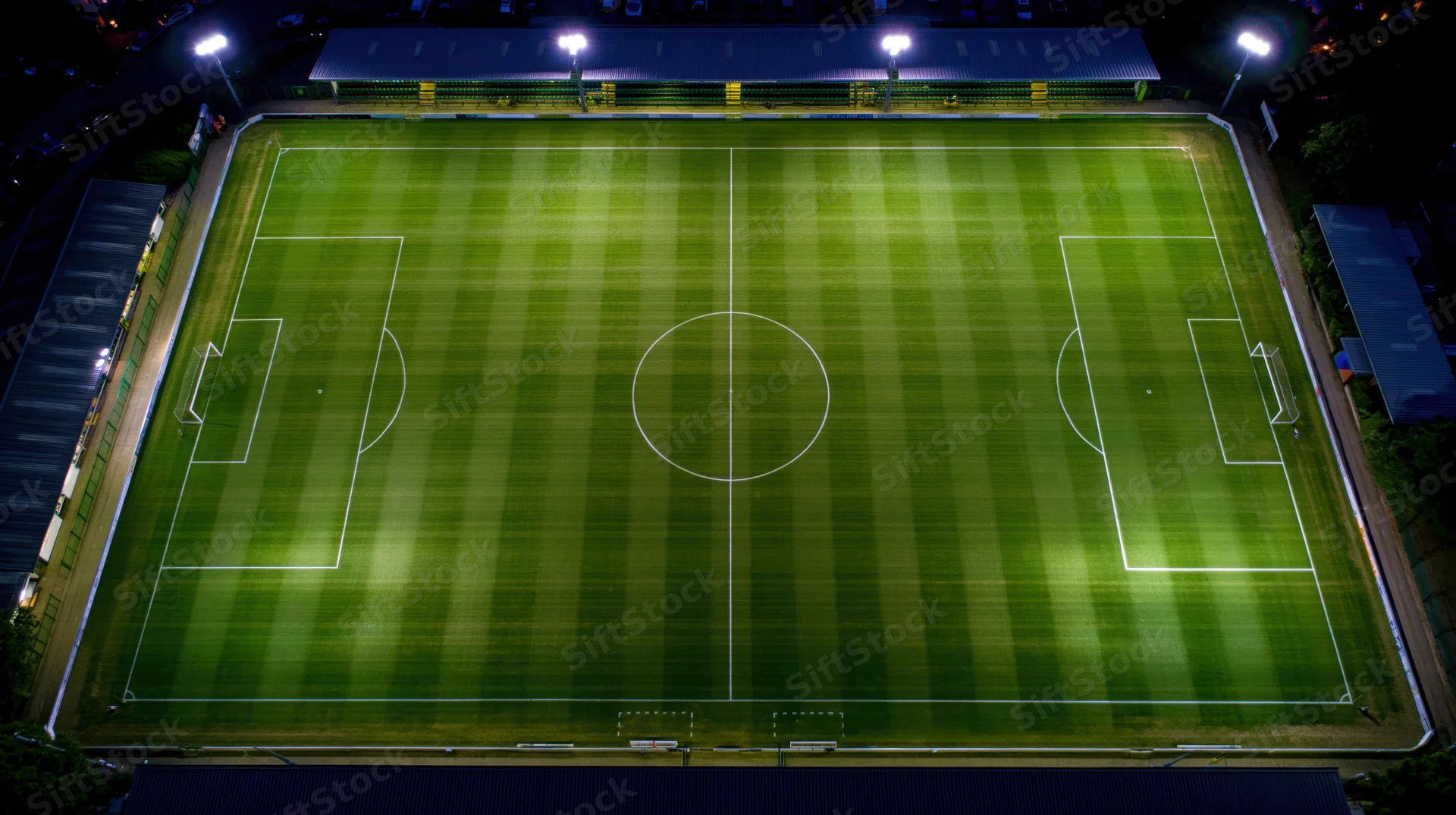 Aerial view of a soccer field at night illuminated by floodlights with striped grass and white markings